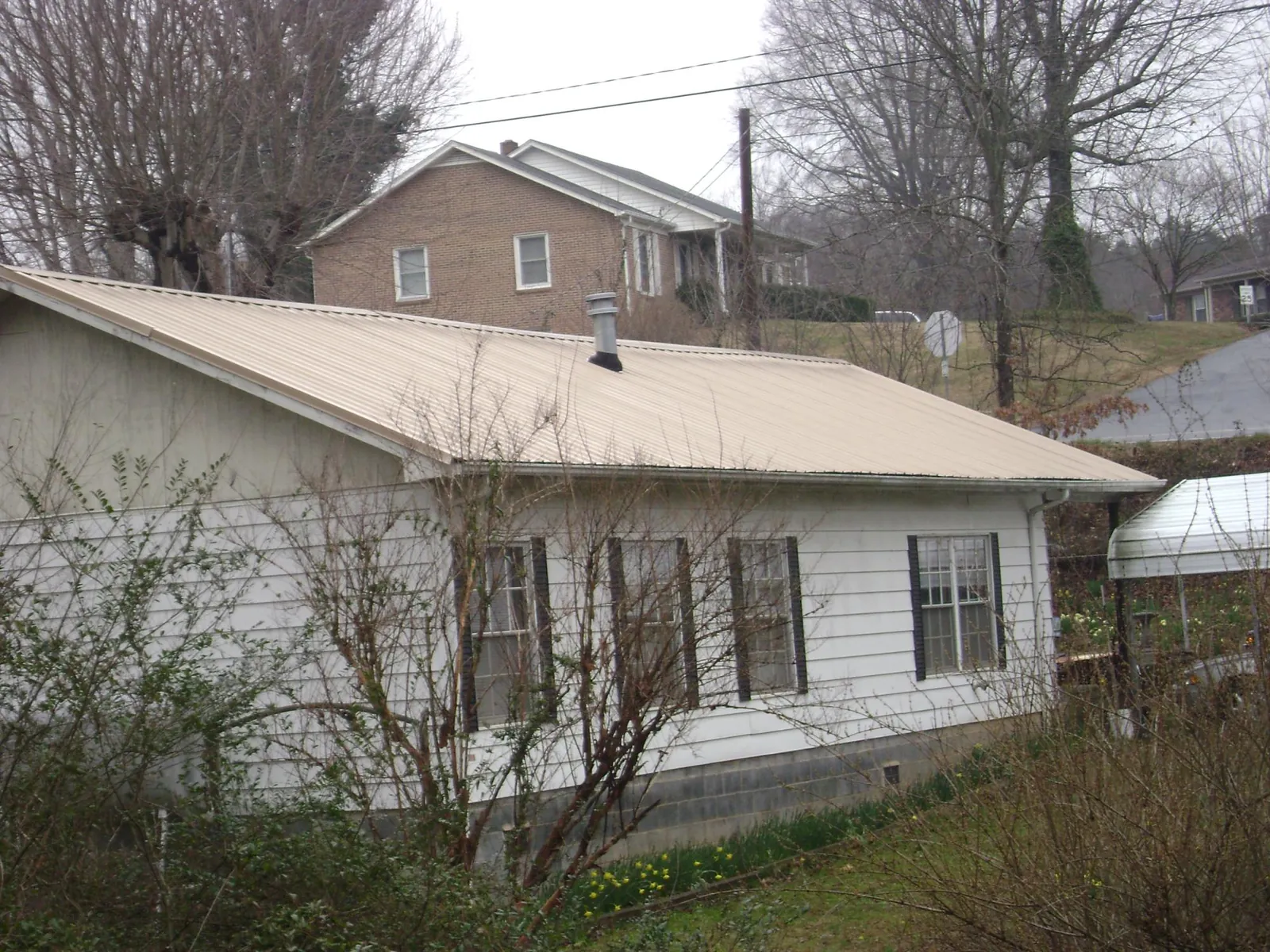Tan metal roof on a white sided house set into a hillside — Commercial Roofing by Roofing Brothers in Somers